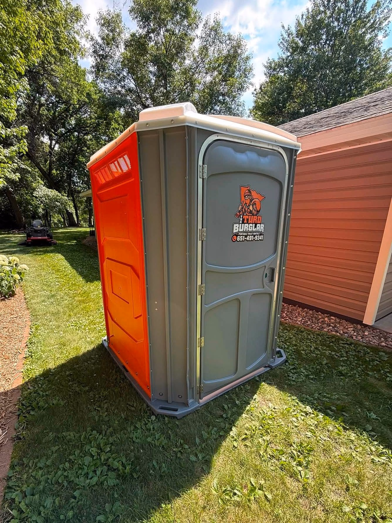 A wide handicapped accessible portable toilet standing on a mown lawn.