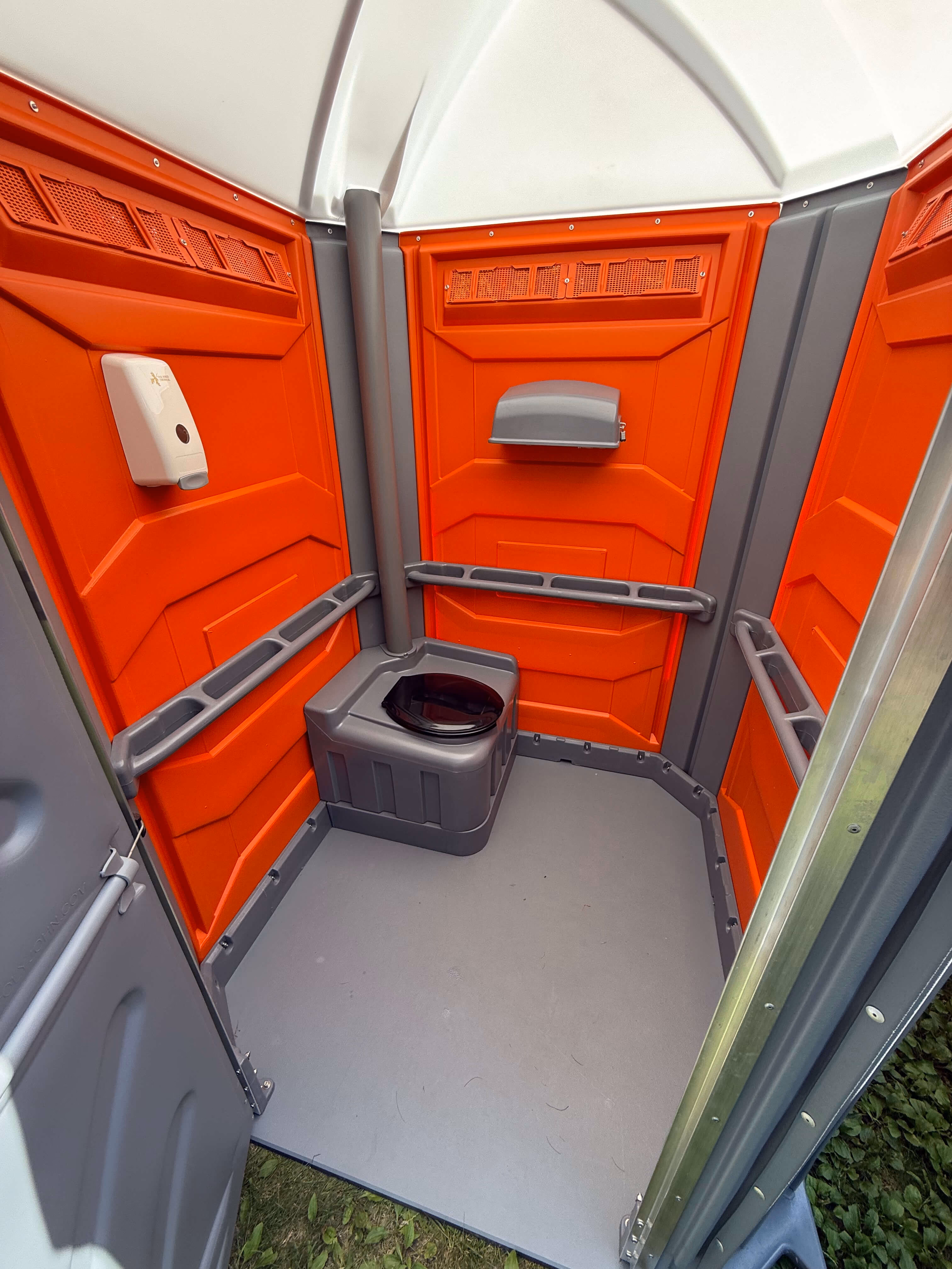 Inside an accessible portable toilet with orange walls and grab bars on both side walls.
